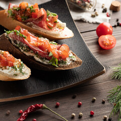 From above yummy bruschettas with bacon served on plate on wooden table near cooking ingredients during lunch