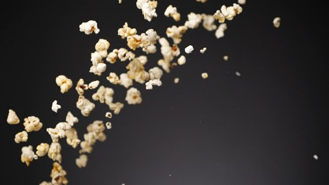 Bunch of crunchy popcorn flying up in air and falling down in slow motion on gray background