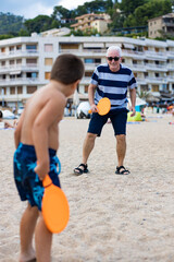 Grandfather and grandson playing tennis on the beach