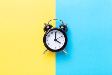 Black alarm clock on two tone color yellow and blue background. Top view, place for text