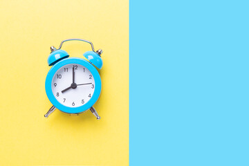 Blue alarm clock on two tone color yellow and blue background. Top view, place for text