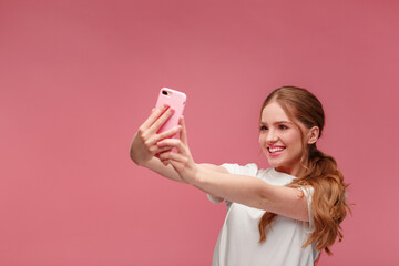 Funny young redhead woman making selfie. Smiling girl wearing white t-shirt holding pink...
