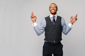 young funny african-american businessman crossing fingers, wishing, hoping for best, miracle over grey background