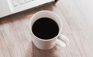 Close up black coffee in white cup and laptop on wooden table. Work from home concept