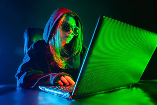 Hacking. Hacker near the laptop. Girl makes a hacker attack. Internet hacking. Concept - a member of a hacker group. Geek in a dark room. Concept - computer geek. Woman in front of a computer.