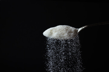 Obraz na płótnie Canvas sugar is poured from a spoon on a black background. Excessive sugar intake. Sweet crystals