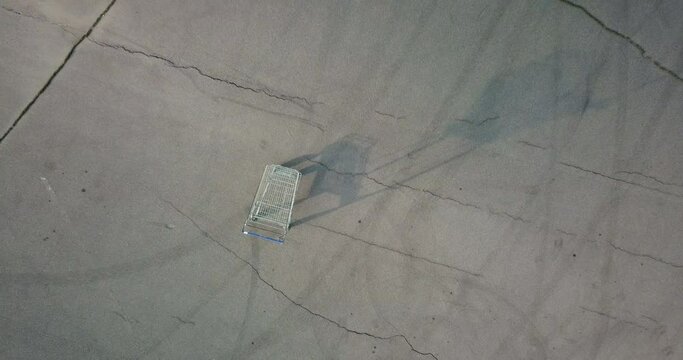 Single empty shopping cart standing on chappy asphalt square, zoom in video, top view