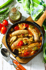 Stew of beans, vegetables and smoked sausages with tomato sauce in the pan on wooden table.