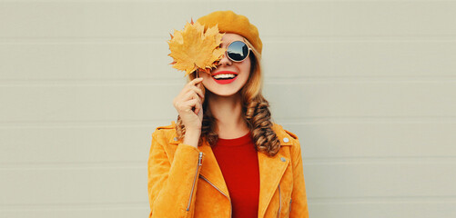 Autumn portrait of happy smiling woman with yellow maple leaves wearing french beret over gray background
