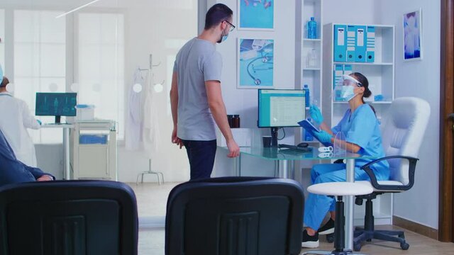 Patient with face mask against coronavirus at hospital reception asking nurse for direction. Handicapped senior woman in wheelchair with sterile face protection against covid-19.