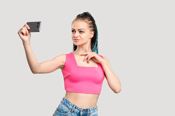 Creative blogger lifestyle. Social media. Confident woman in pink with dyed braids hairstyle taking selfie on smartphone camera isolated on neutral copy space. Mobile app. Internet promotion.