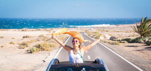 one young woman enjoying and having fun in their vacations outdoors - female person in freedom concept and lifestyle with a car in the middle of the road woth the ocean or sea at the background © simona