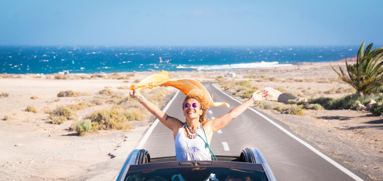one young woman enjoying and having fun in their vacations outdoors - female person in freedom concept and lifestyle with a car in the middle of the road woth the ocean or sea at the background