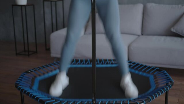 Athletic woman enjoys home workouts and jumps to music on a trampoline