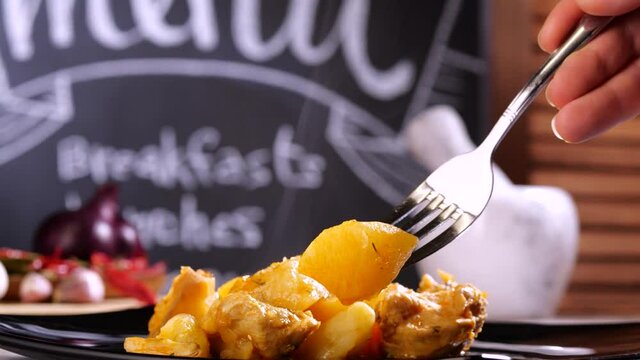 Tilt up view of anonymous person taking piece of tasty roasted potato from plate while having lunch in cafe