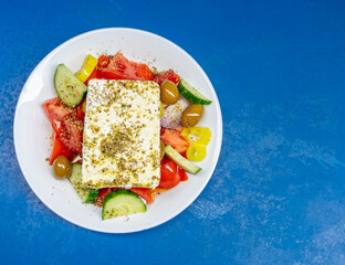 fresh Greek salad plate top view on vibrant blue table background, space for text