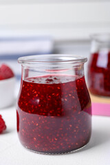 Delicious raspberry jam in jar on white table, closeup