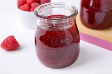 Delicious jam and fresh raspberries on white table, closeup