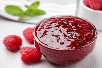 Delicious jam and fresh raspberries on white table, closeup