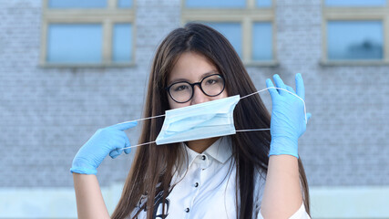 A schoolgirl wearing medical gloves and wearing a mask stands in front of the school. A high school student wearing protective gloves holds a medical mask. The girl in the defense smiles.