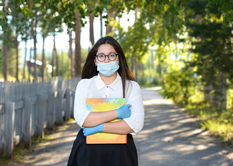 A schoolgirl wearing a medical mask against a green tree. A high school student stands in a school alley. A girl in protective equipment holds a school textbook.