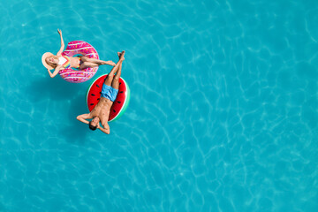 Happy couple with inflatable rings in swimming pool, top view and space for text. Summer vacation