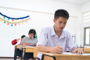 Fototapeta premium Young Asian students group writing exam on test paper answer sitting on taking final examination in classroom with concentration, Test in high school /university student in exams room