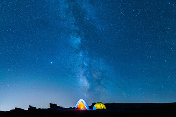 Camping in the mountains under the starry sky and the vastness of the universe. Milky Way in the starry night sky with bright tents below.