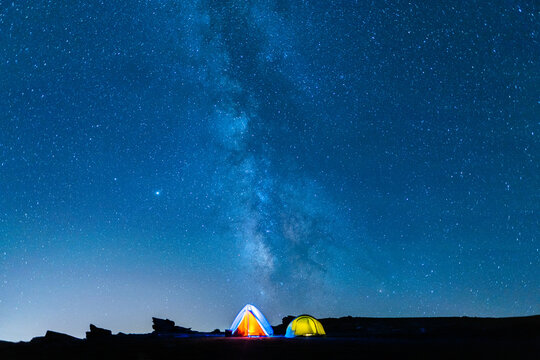 Camping In The Mountains Under The Starry Sky And The Vastness Of The Universe. Milky Way In The Starry Night Sky With Bright Tents Below.