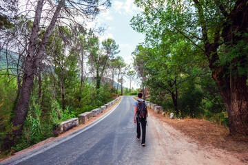 Fototapeta na wymiar Young adventurer on his back with backpack walking while traveling on nature tourism on a road in the middle of the forest in the Cazorla Natural Park, in Spain. Selective focus.