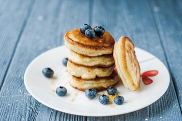 Close-up delicious pancakes, with fresh blueberries and maple syrup on a light background. With copy space. Sweet maple syrup flows from a stack of pancake