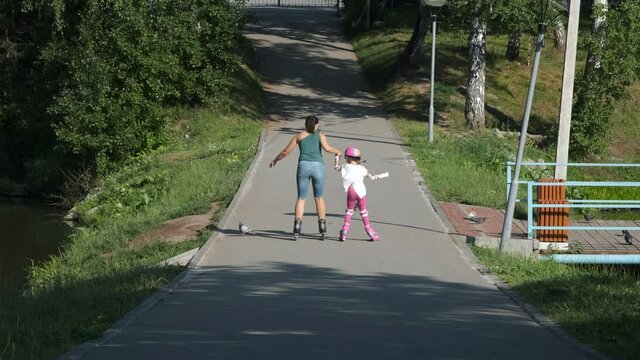 Little Girl in Protection Pads and Colorful Helmet Falling while Roller Skating with Mother in a Park. Childhood, Summer Activities and Healthy Lifestyle Concept