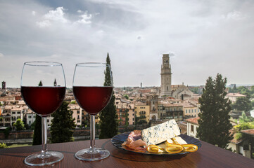 Two glasses of wine with charcuterie assortment on view of Verona, Italy. Glass of red wine with...