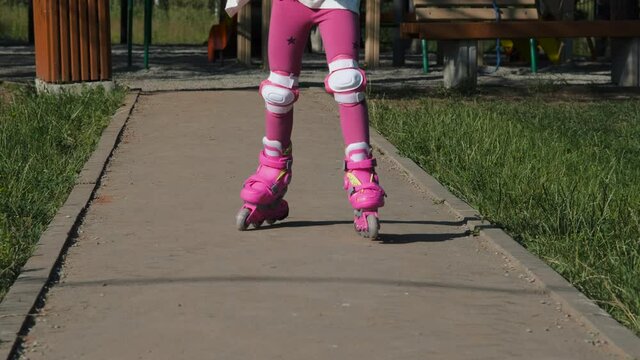 Close-up of Little Girl in Protection Pads Learning Roller Skating in a City Park. Slow Motion. Childhood, Summer Activities and Healthy Lifestyle Concept