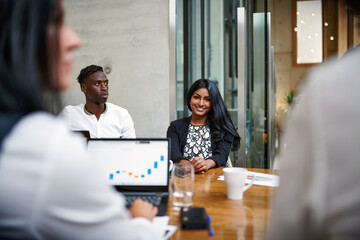 Portrait of smiling young businesswoman sitting amidst colleagues at conference table in creative office during meeting
