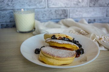 pancakes with berries and powdered sugar on a white plate and a glass of milk