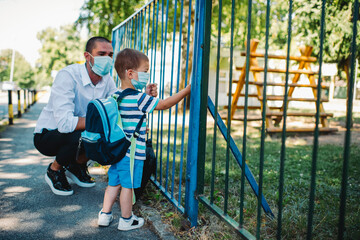 Business father and son going to kindergarten. They are wearing a medical face masks.