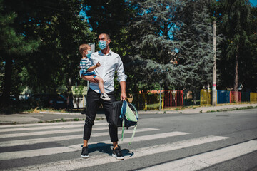 Young businessman taking  son to  kindergarten. They are wearing a medical face mask.