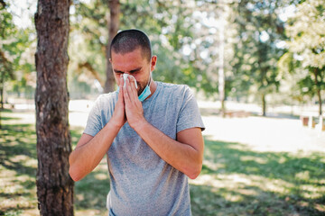 Young man uses tissue paper sneezing due to having allergy. Young man wear face mask and  sneezing outdoors