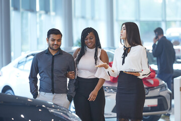 Obraz premium Visiting a car dealership choosing and buying a new car a young emotional African-American couple communicates in with a car sales Manager. Selective focus.