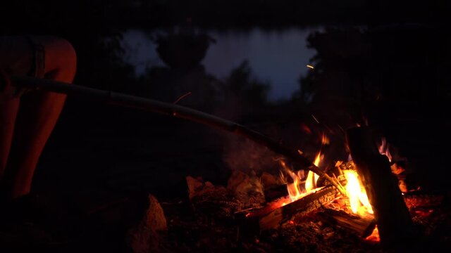 The man straightens the coals in the fire. The fire is burning in the middle of the night close-up.