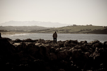 Persona solitaria observando la playa de Liencres desde las rocas.