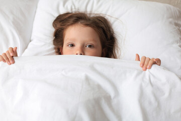 Cute child little girl woke up and lies in the bed.