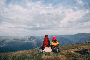 Fototapeta premium Two guys are sitting and looking into the distance and the mountains, discussing something and showing somewhere far into the distance with his hand.