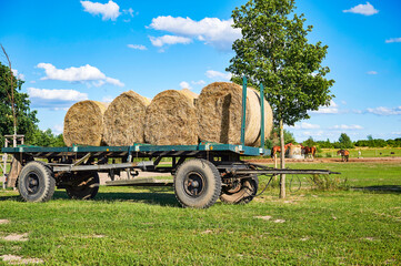Obraz premium An old trailer with bales of straw standing in a meadow.