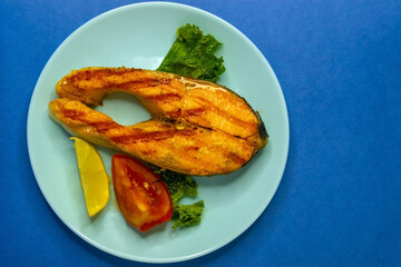 Large fish steak on a blue plate with vegetables