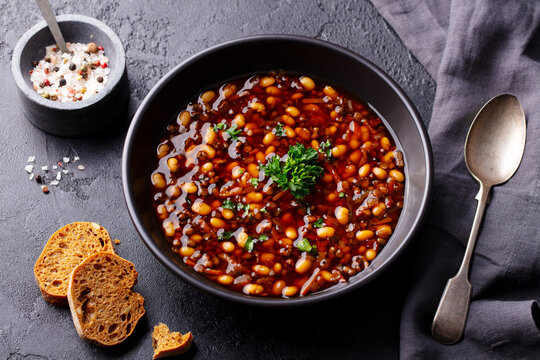 Bean soup in a black bowl. Grey background. Close up.