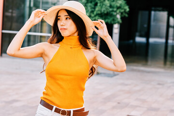 asian girl using a hat in an urban environment on a summer day