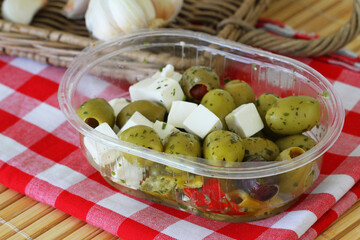 Green olives and pieces of feta cheese in transparent plastic box
