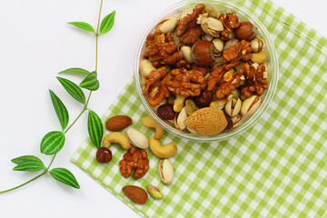 Pistachios, walnuts, cashew nuts, hazelnuts, peanuts, almonds in bowl on green and white checkered cloth
